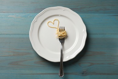 Photo of Heart made of tasty spaghetti and fork on light blue wooden table, top view