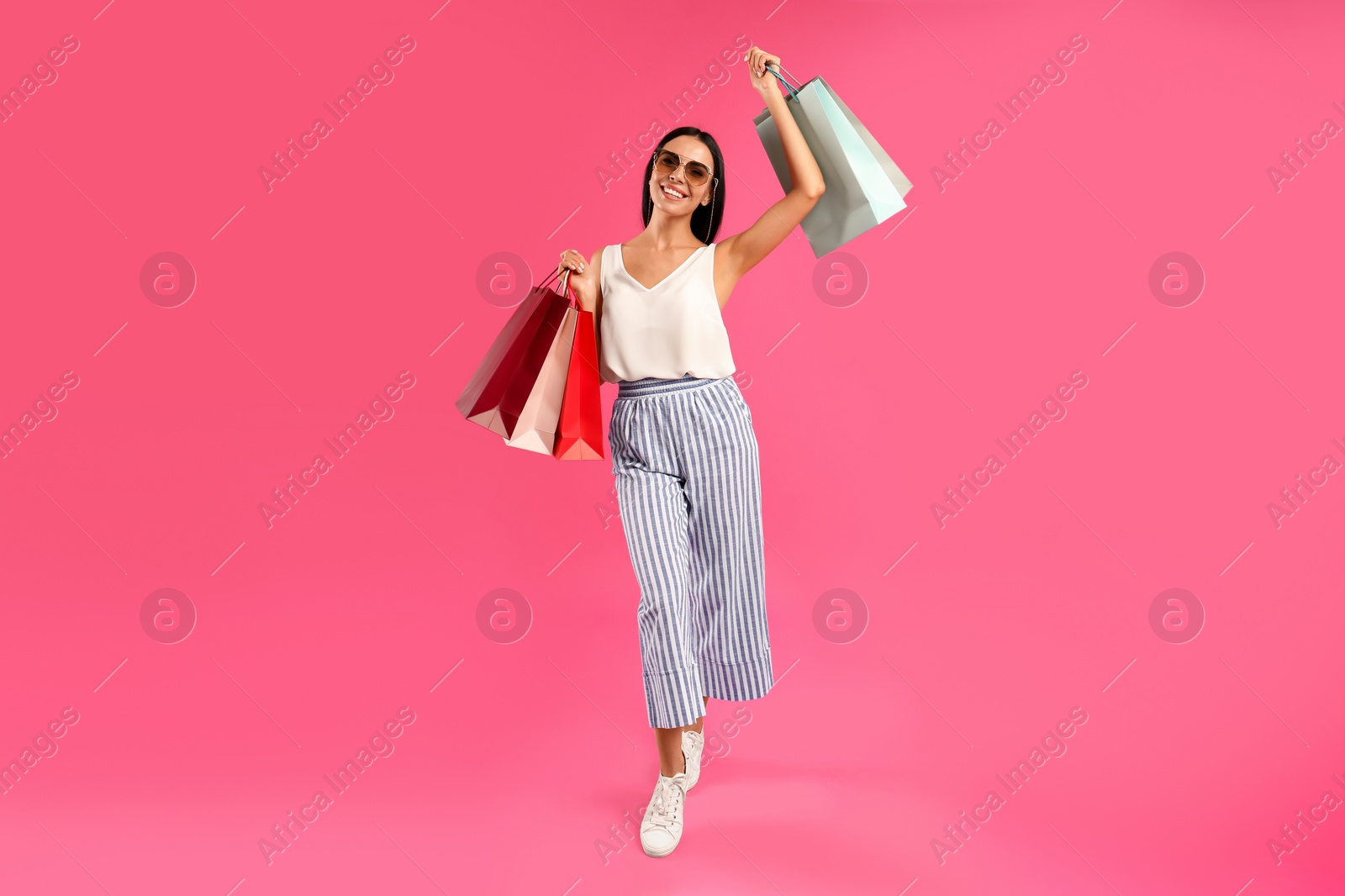 Photo of Beautiful young woman with paper shopping bags on pink background