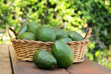 Photo of Wicker basket with fresh ripe avocados on wooden table outdoors