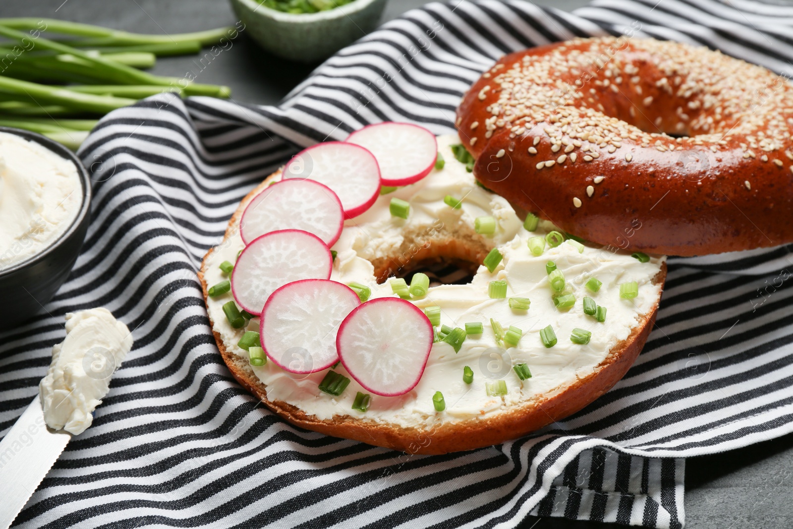 Photo of Delicious bagel with cream cheese, green onion and radish on table, closeup