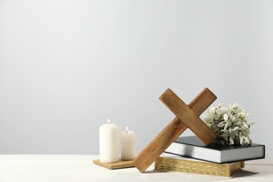 Burning church candles, wooden cross, ecclesiastical books and flowers on white table. Space for text