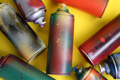 Many spray paint cans on yellow background, flat lay