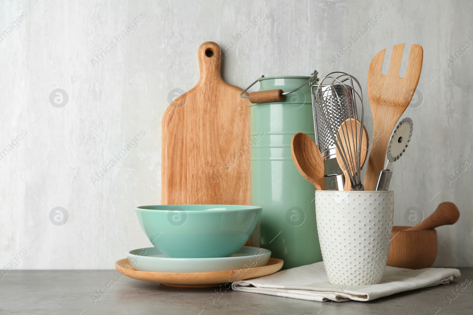 Photo of Different kitchen utensils on grey table against light background