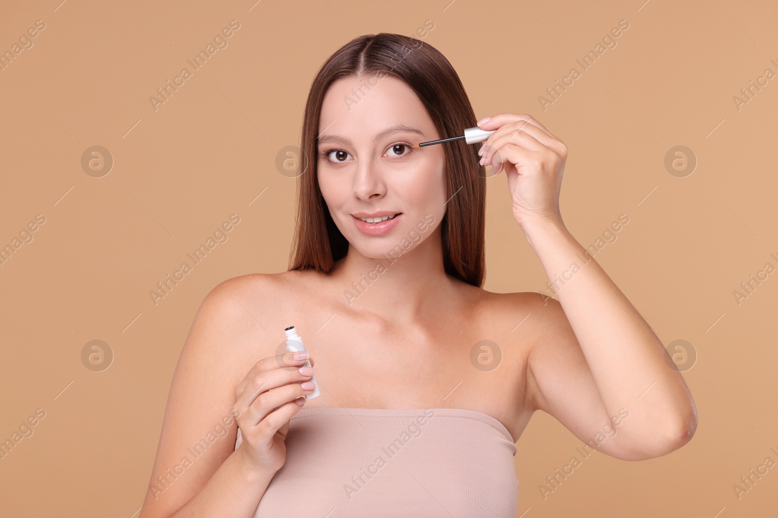 Photo of Beautiful woman applying serum onto eyelashes on beige background