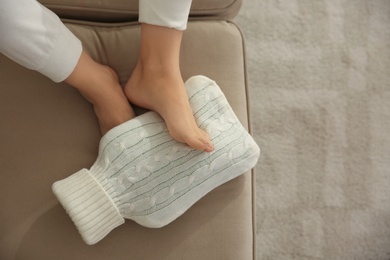 Woman warming feet with hot water bottle on sofa, closeup