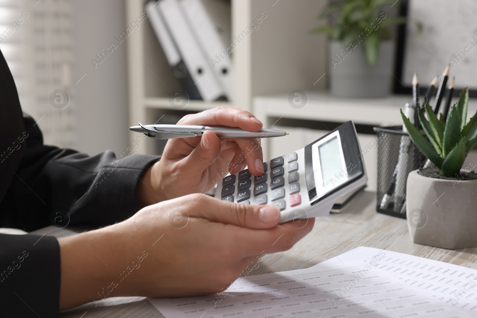 Photo of Woman using calculator at light wooden table in office, closeup