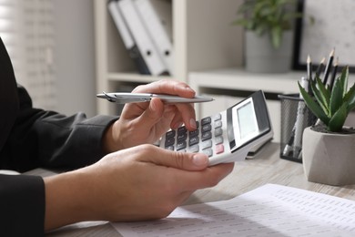 Photo of Woman using calculator at light wooden table in office, closeup