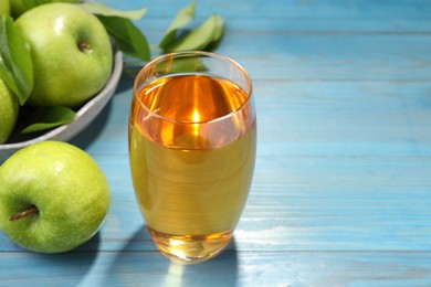 Photo of Glass of fresh juice and apples on light blue wooden table, closeup. Space for text