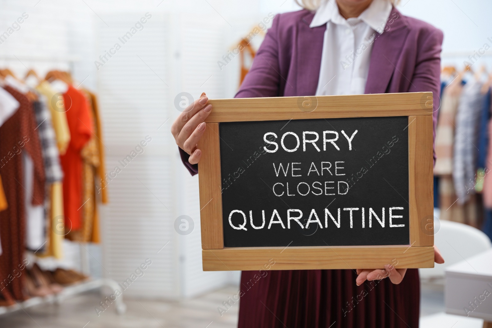 Image of Business owner holding sign with text SORRY WE ARE CLOSED QUARANTINE in boutique, closeup