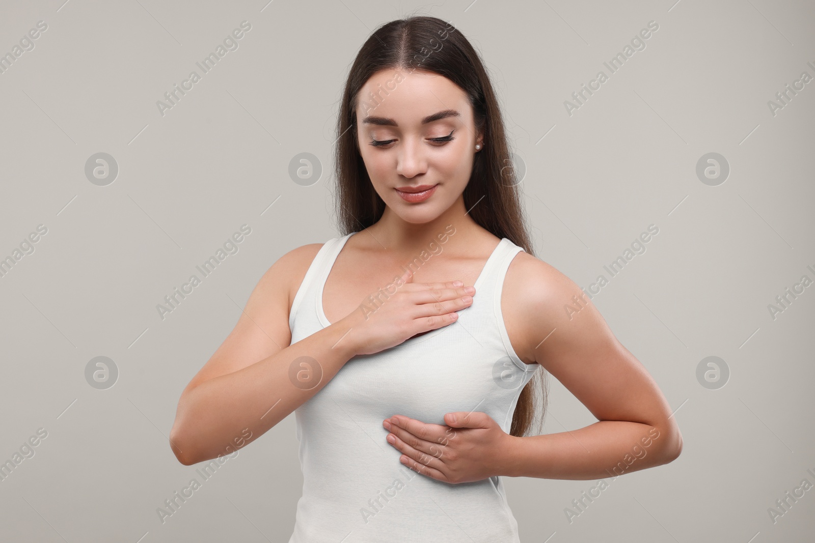 Photo of Beautiful young woman doing breast self-examination on light grey background