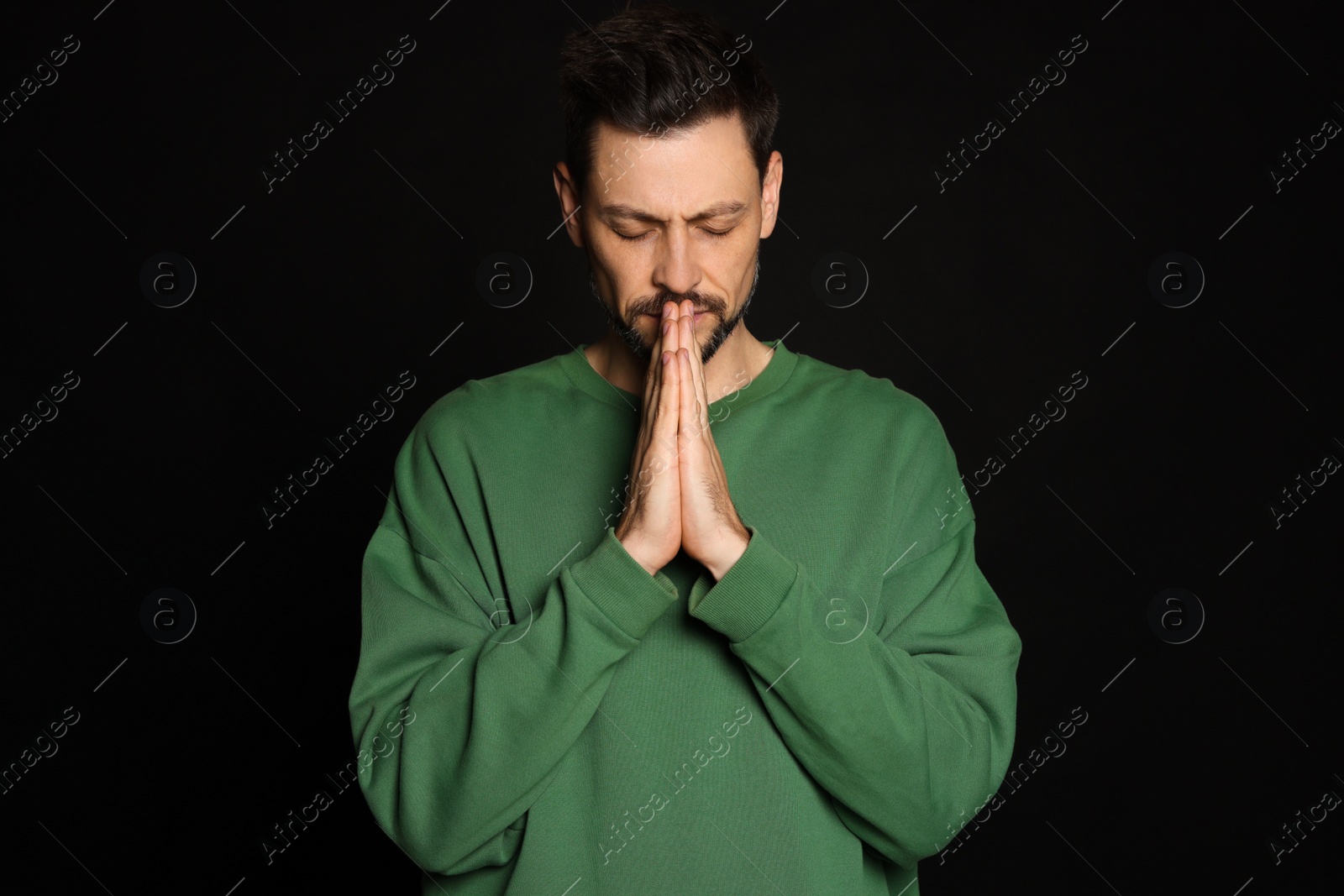 Photo of Man with clasped hands praying on black background