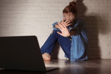 Photo of Scared teenage girl with laptop on floor in dark room. Danger of internet