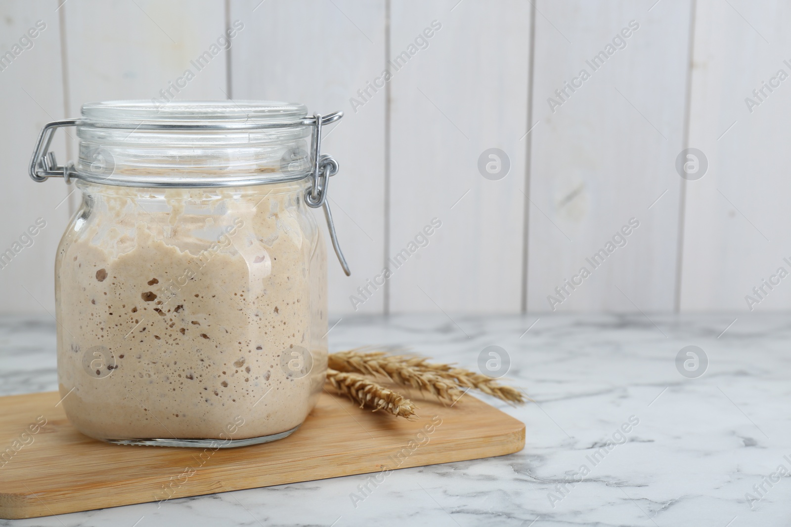 Photo of Leaven and ears of wheat on white marble table, space for text