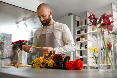 Photo of Florist making bouquet with fresh flowers at table in shop