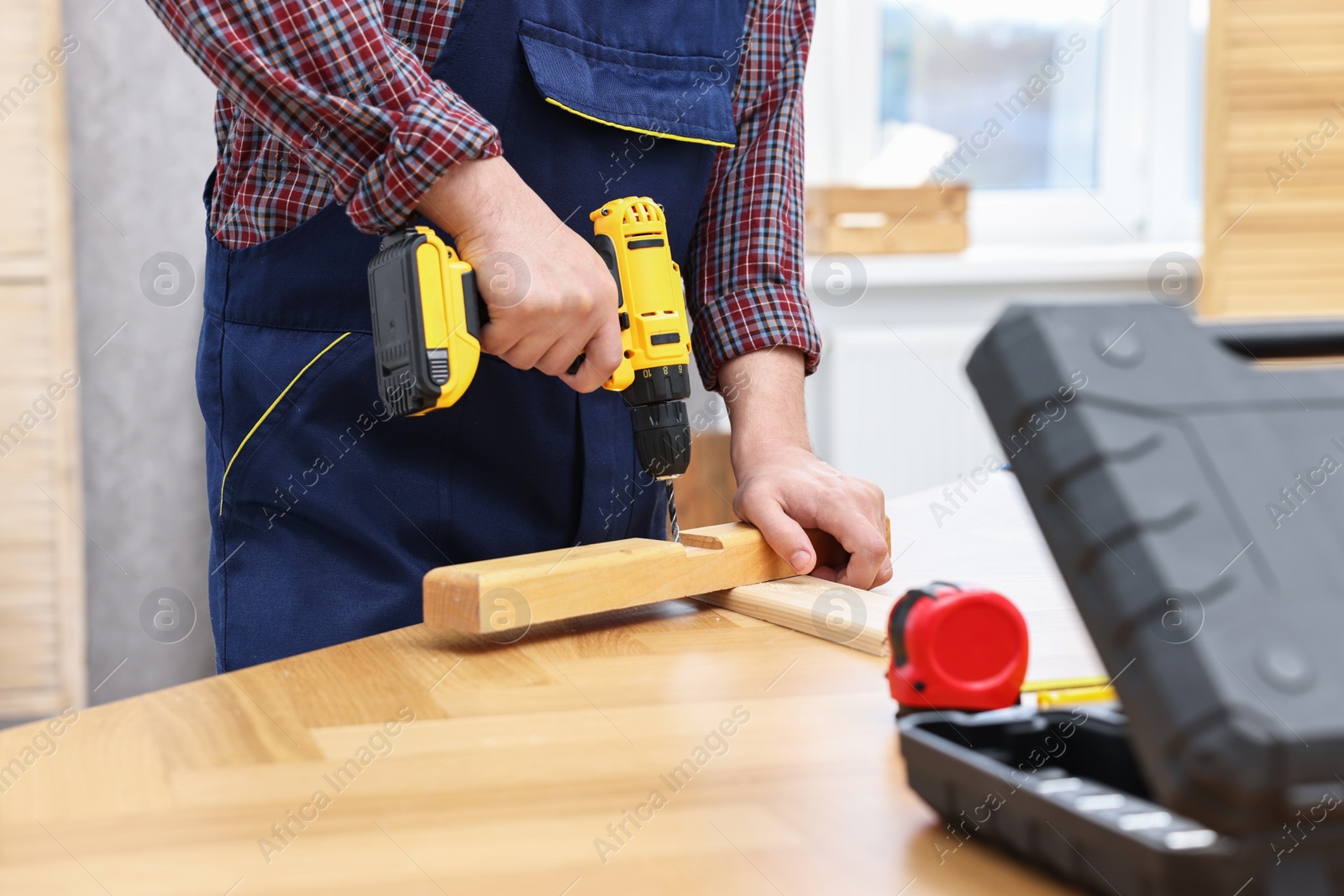 Photo of Young worker using electric drill at table in workshop, closeup