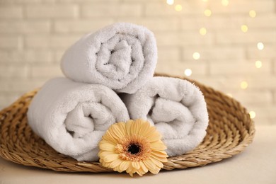 Photo of Rolled terry towels and flower on white table near brick wall indoors, closeup