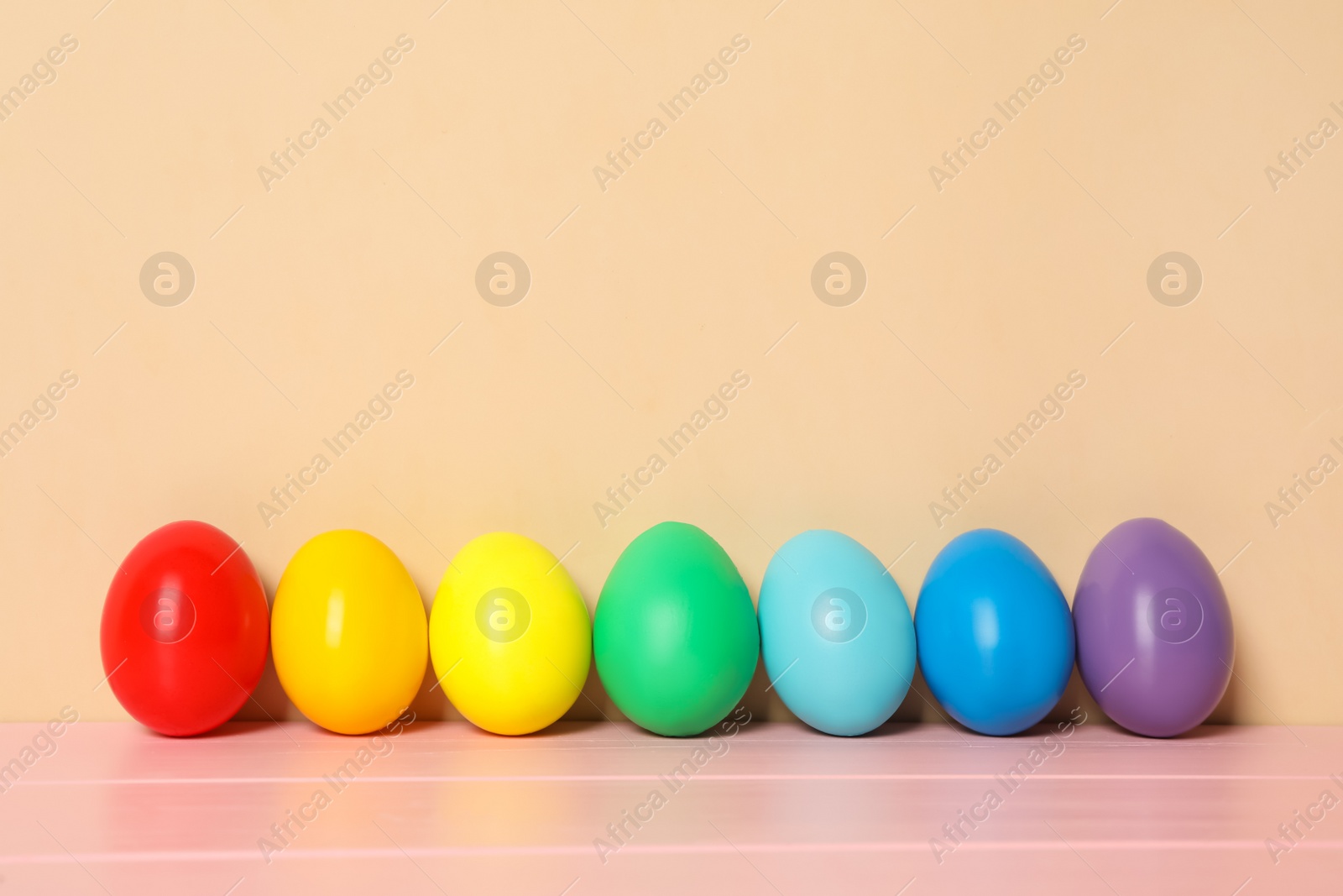 Photo of Easter eggs on pink wooden table against beige background, space for text
