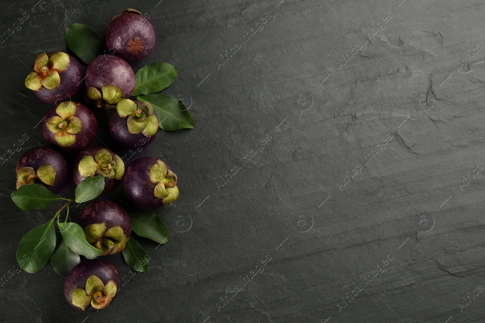 Photo of Fresh ripe mangosteen fruits on dark grey table, flat lay. Space for text