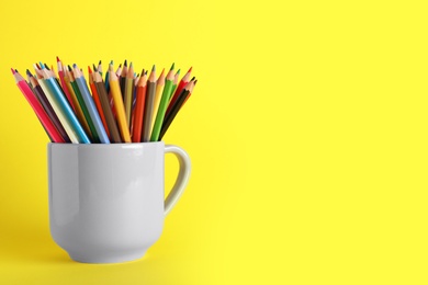 Photo of Colorful pencils in light cup on yellow background. Space for text