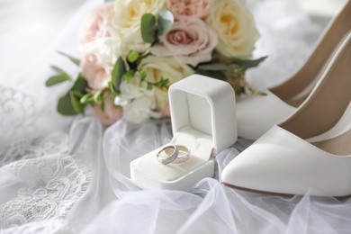 Photo of Pair of white high heel shoes, rings and wedding bouquet on lace veil