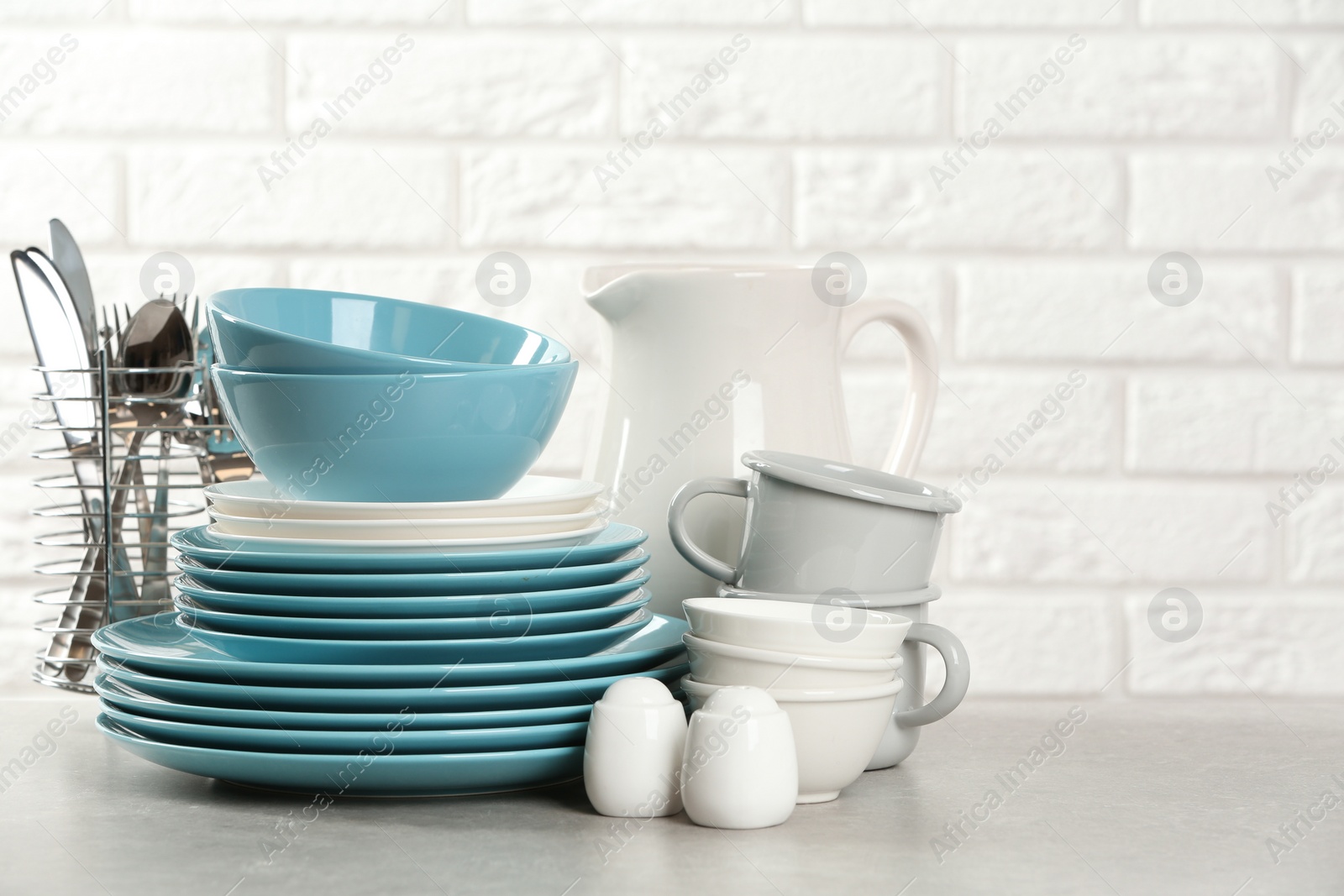 Photo of Set of clean dishes on table near brick wall. Space for text