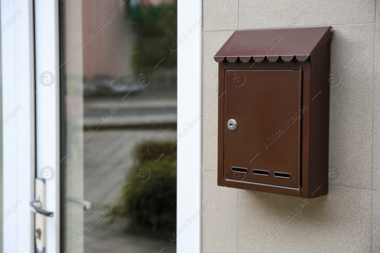 Photo of Brown metal letter box on light grey wall, space for text