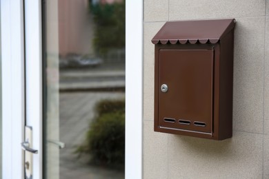 Photo of Brown metal letter box on light grey wall, space for text