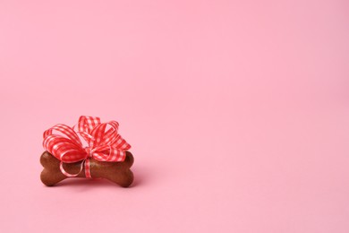Photo of Bone shaped dog cookie with red bow on pink background, space for text