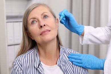 Photo of Medical drops. Doctor dripping medication into woman's ear indoors