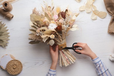 Florist making beautiful bouquet of dried flowers at white table, top view