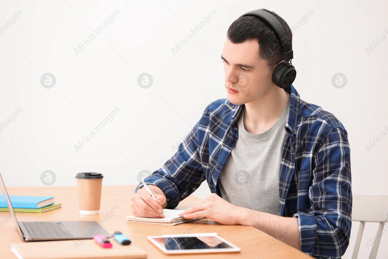 Photo of E-learning. Young man taking notes during online lesson at table indoors.