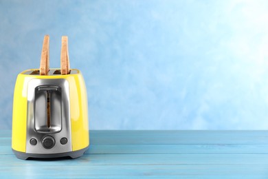 Photo of Modern toaster with slices of bread on light blue wooden table. Space for text