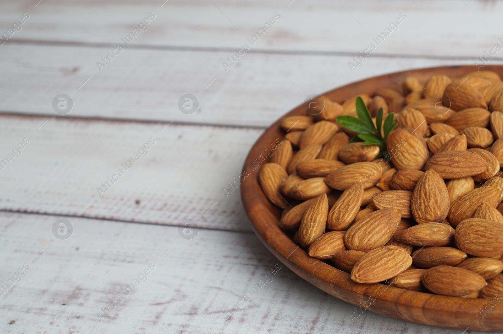 Photo of Plate with tasty almonds on white wooden table. Space for text