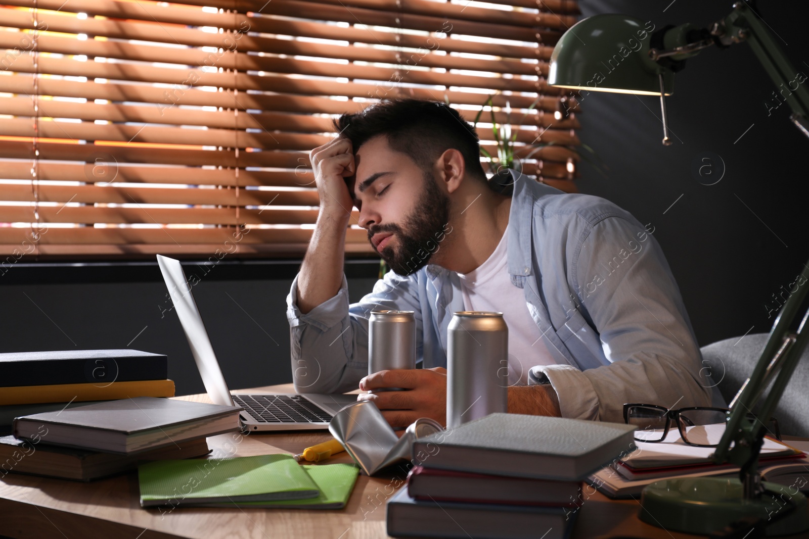 Photo of Tired young man with energy drink studying at home