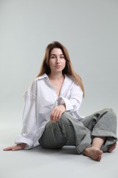 Portrait of beautiful young woman sitting on grey background
