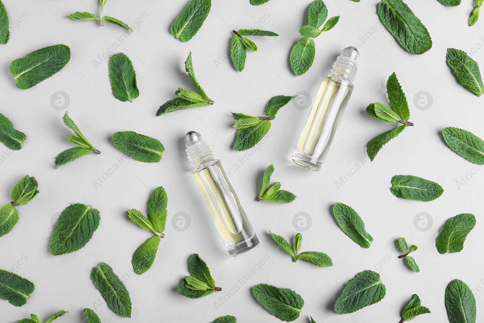 Photo of Glass bottles with essential oil among mint leaves on light background, flat lay