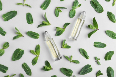 Glass bottles with essential oil among mint leaves on light background, flat lay