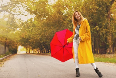 Photo of Beautiful young woman wearing stylish autumn clothes with red umbrella in park