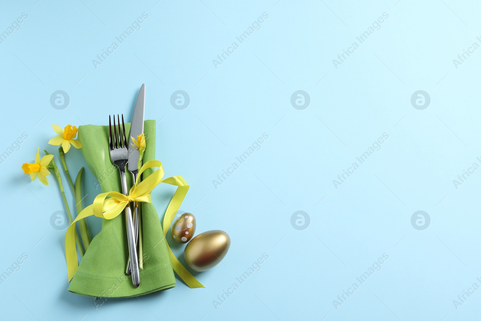 Photo of Cutlery set, Easter eggs and narcissuses on light blue background, flat lay with space for text. Festive table setting