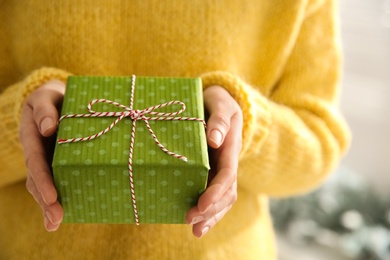 Photo of Woman holding green Christmas gift box indoors, closeup