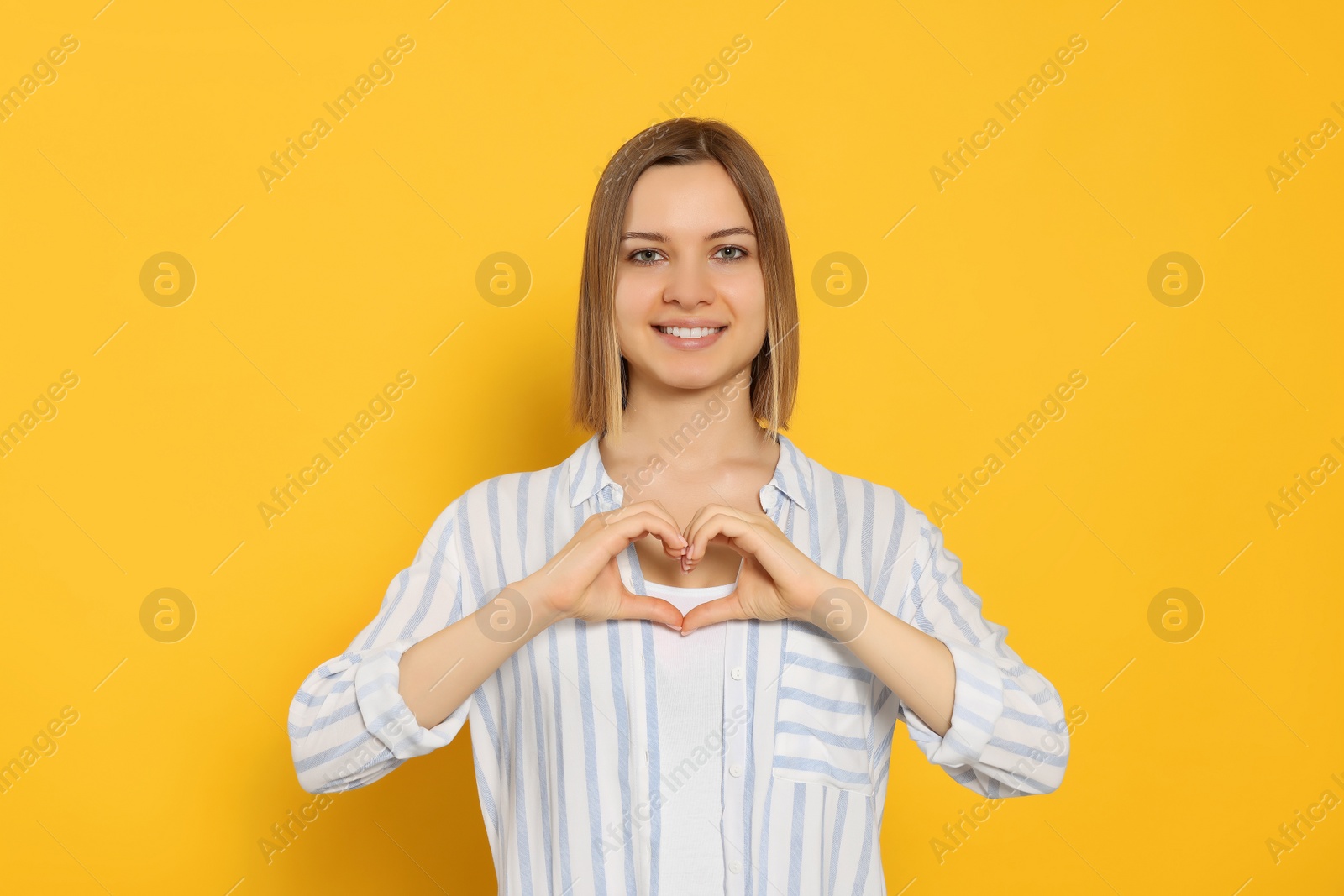 Photo of Young woman making heart with hands on yellow background. Volunteer concept