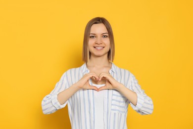 Photo of Young woman making heart with hands on yellow background. Volunteer concept