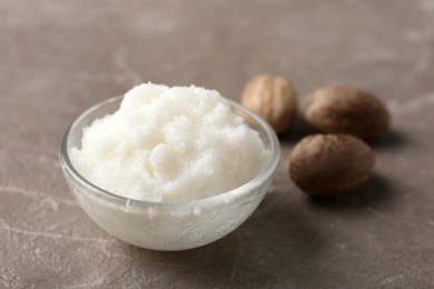 Shea butter in bowl and nuts on grey background, closeup