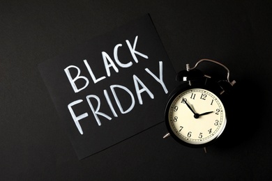 Photo of Phrase Black Friday and alarm clock on dark background, flat lay