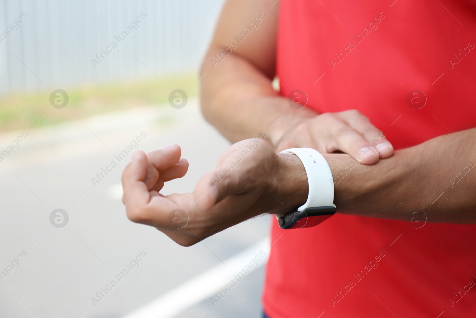 Photo of Young man checking pulse after training outdoors, closeup