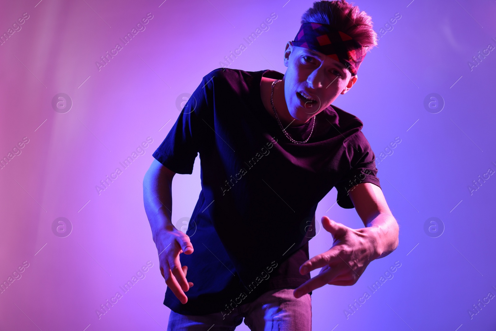 Photo of Stylish young man on color background in neon lights, low angle view