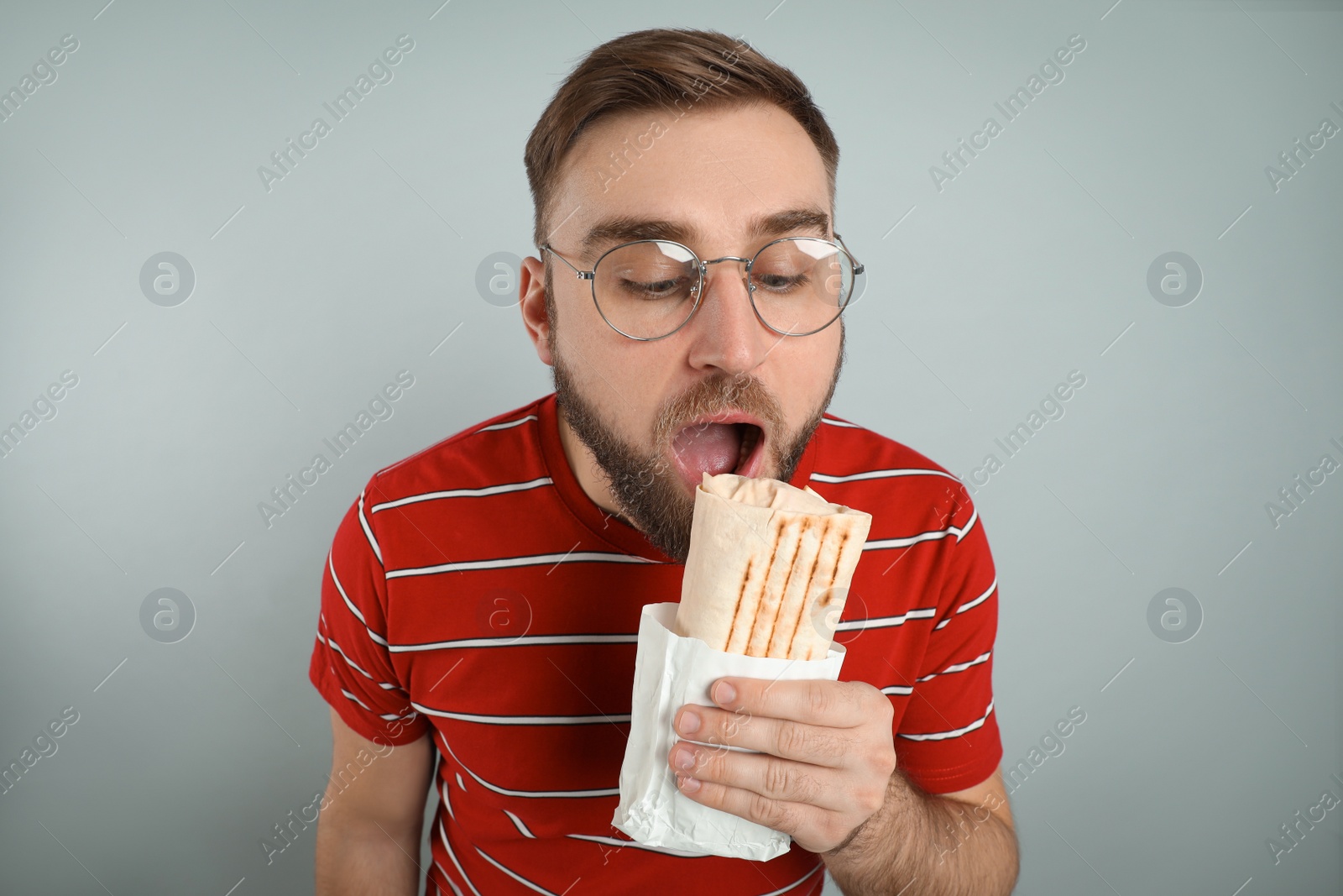 Photo of Young man eating delicious shawarma on grey background