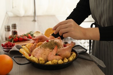 Photo of Woman cooking Chicken with orange and potato slices at wooden table, closeup