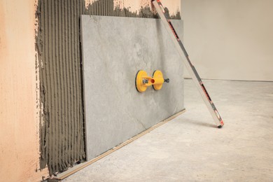 Photo of Construction level and yellow suction plate attached to tile on wall indoors