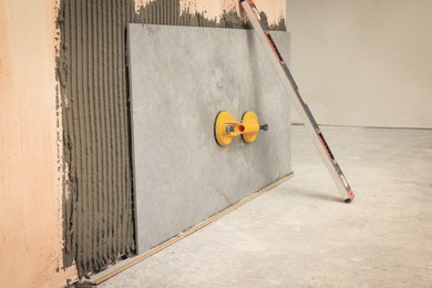 Construction level and yellow suction plate attached to tile on wall indoors